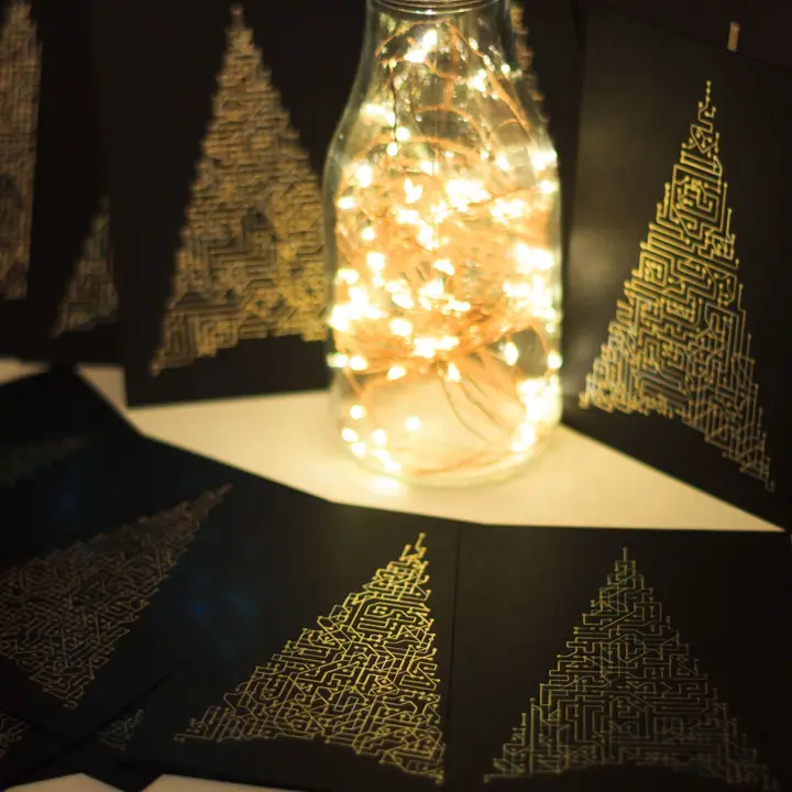 Back cards with a circuit-like maze of interconnected metallic lines at 90 and 45-degree angles, filling the outline of a stylised fir tree, arranged around a glass bottle filled with small fairy lights in a dark room.
